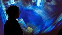 A woman standing in front of a screen with a projection of the scan of the Writtle Hut interior.  preview