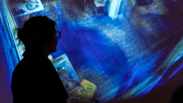 A woman standing in front of a screen with a projection of the scan of the Writtle Hut interior. 