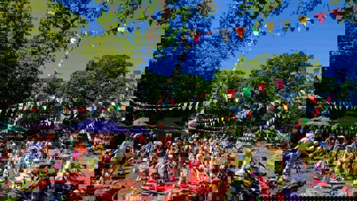 Children and adults playing and having run on rugs laid out on the grass, with bunting string overhead