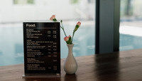 Small food menu sitting on wooden table with small white vase containing carnations, with a view of swimming pool behind preview
