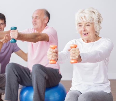 Man coaching older people who are sitting on exercise balls and using hand weights