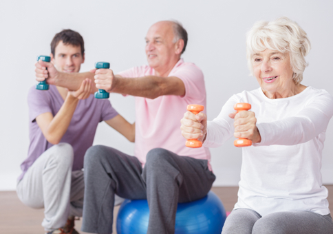 Man coaching older people who are sitting on exercise balls and using hand weights