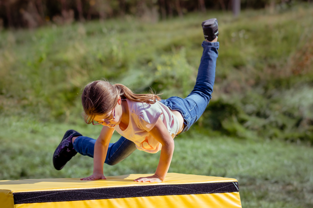 Girl outdoors, jumping over large yellow block