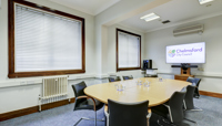 Small meeting room set up with one central meeting table and chairs, with large screen preview