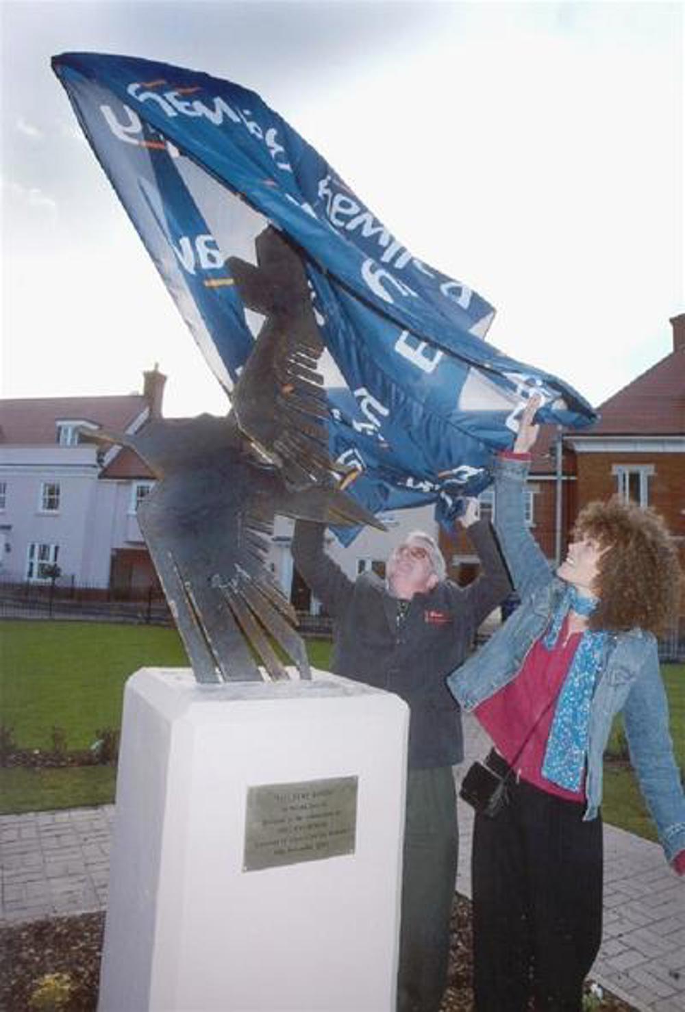 Two women unveiling a sculpture of a bird on a plinth