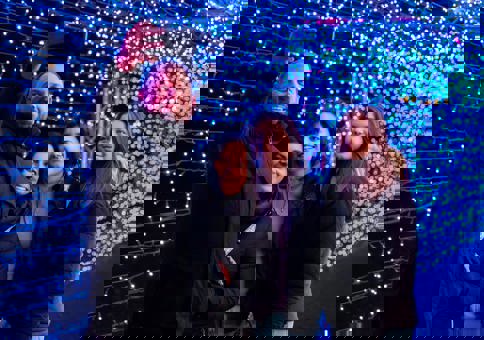 Family with older daughters taking a selfie in a walkway filled with blue fairy lights