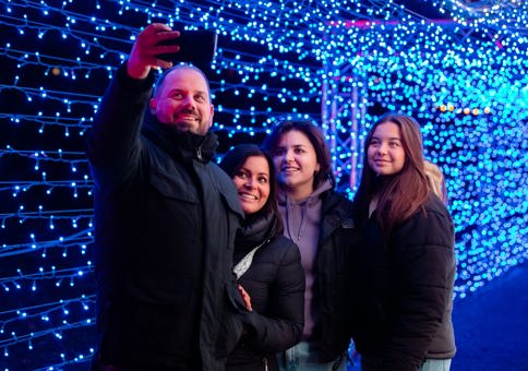 Family with older daughters taking a selfie in a walkway filled with blue fairy lights