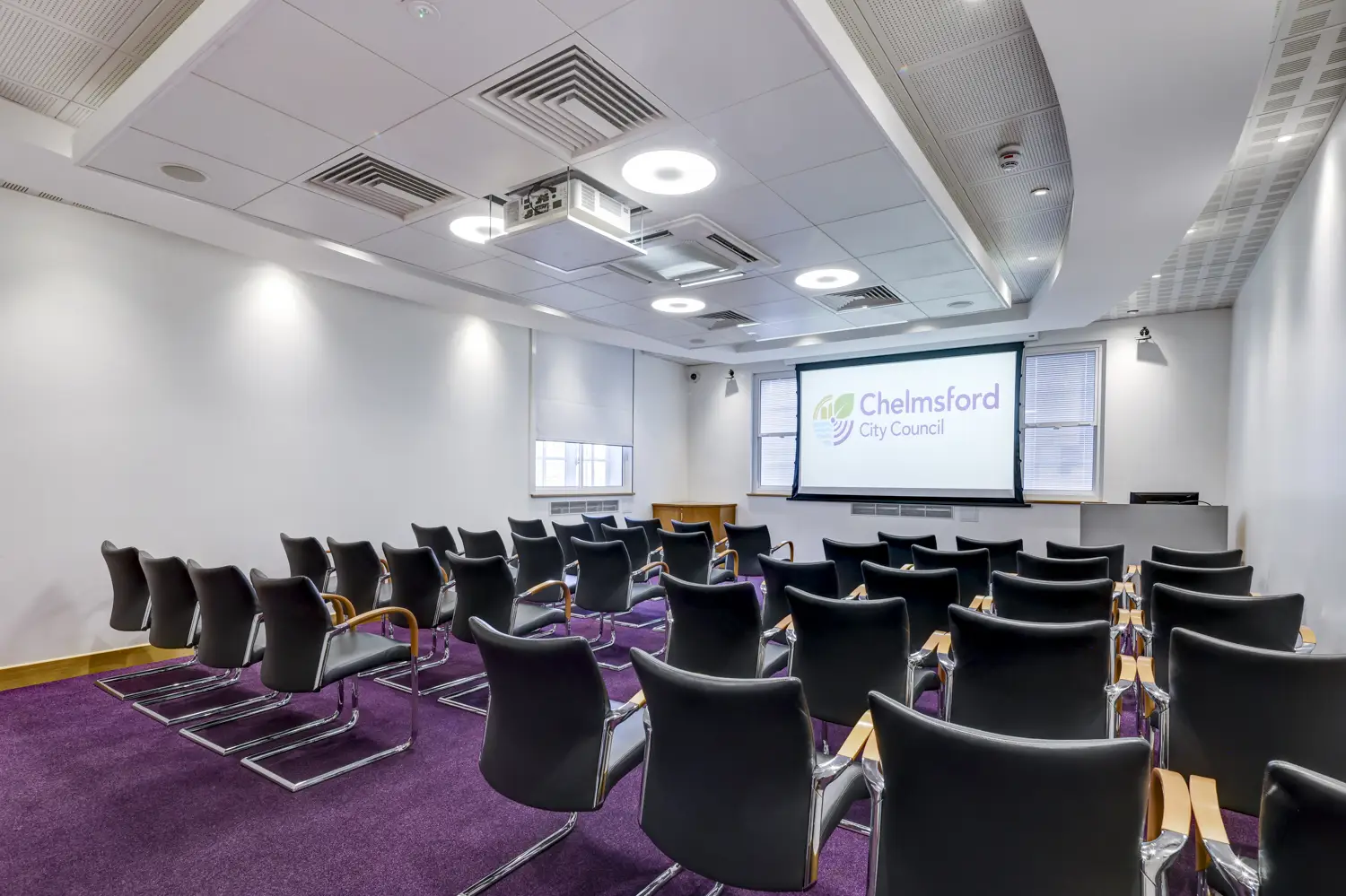 Meeting room set out with audience-style seating, facing large screen