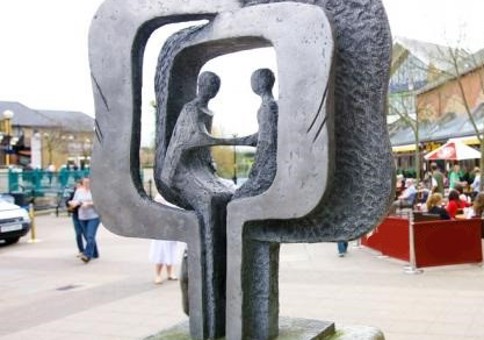 A sculpture of two people sitting, facing each other and holding hands, both surrounded by two square frames, commemorating the 10 year friendship between Chelmsford and Backnang.