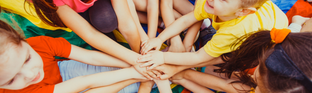 Group of children in a circle, putting their hands together in the middle