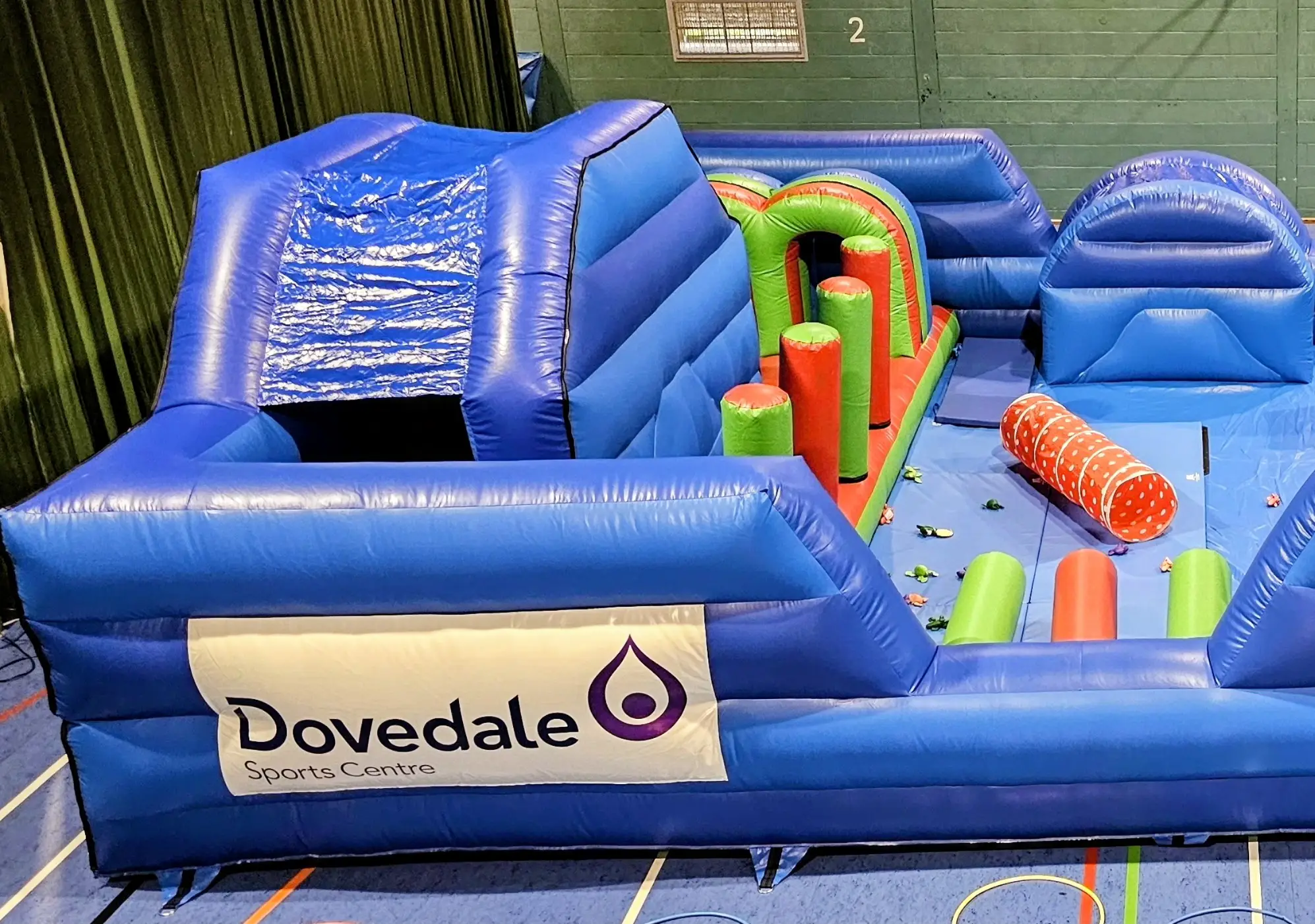 Large blue inflatable in sports hall, with obstacle course inside and Dovedale branding on the outside