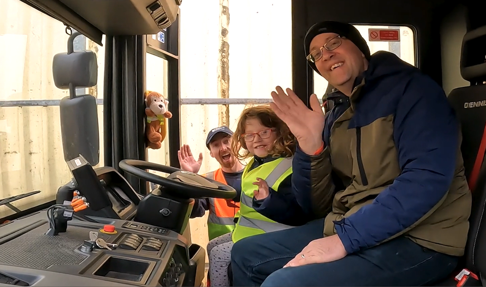 Man and young girl sitting in cab of recycling truck accompanied by male member of staff