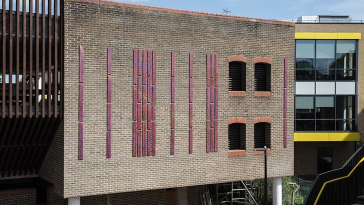 Tall, vertical, copper panels on outside brick wall of car park