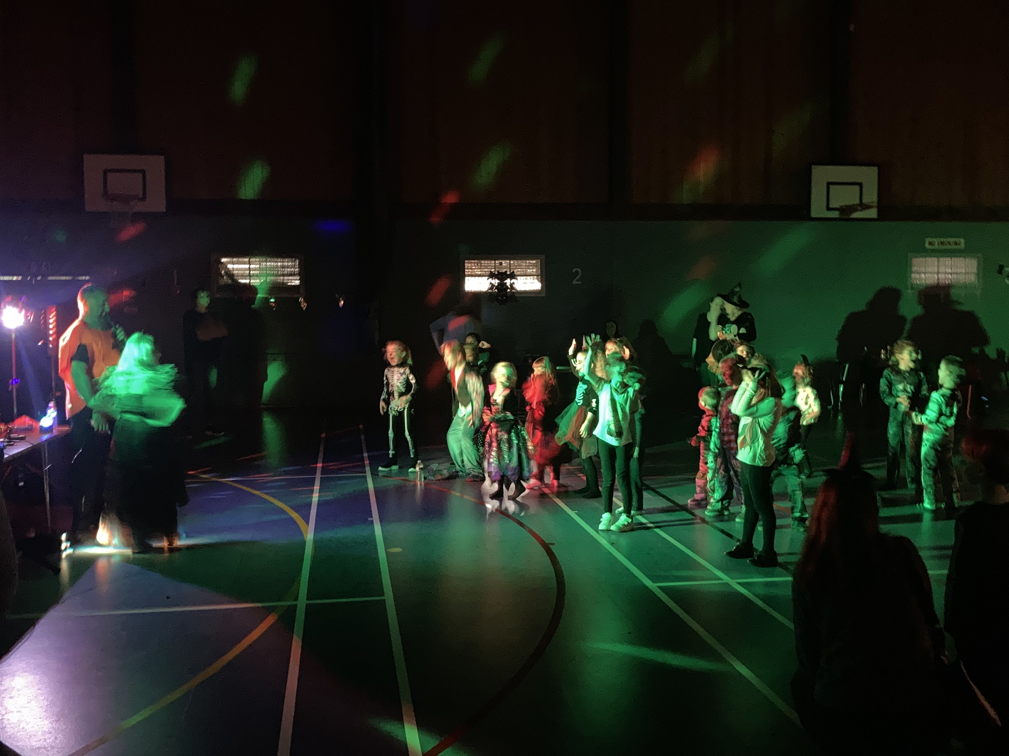 Kids dressed up in a sports hall for Halloween with lights turned down for spooky atmosphere