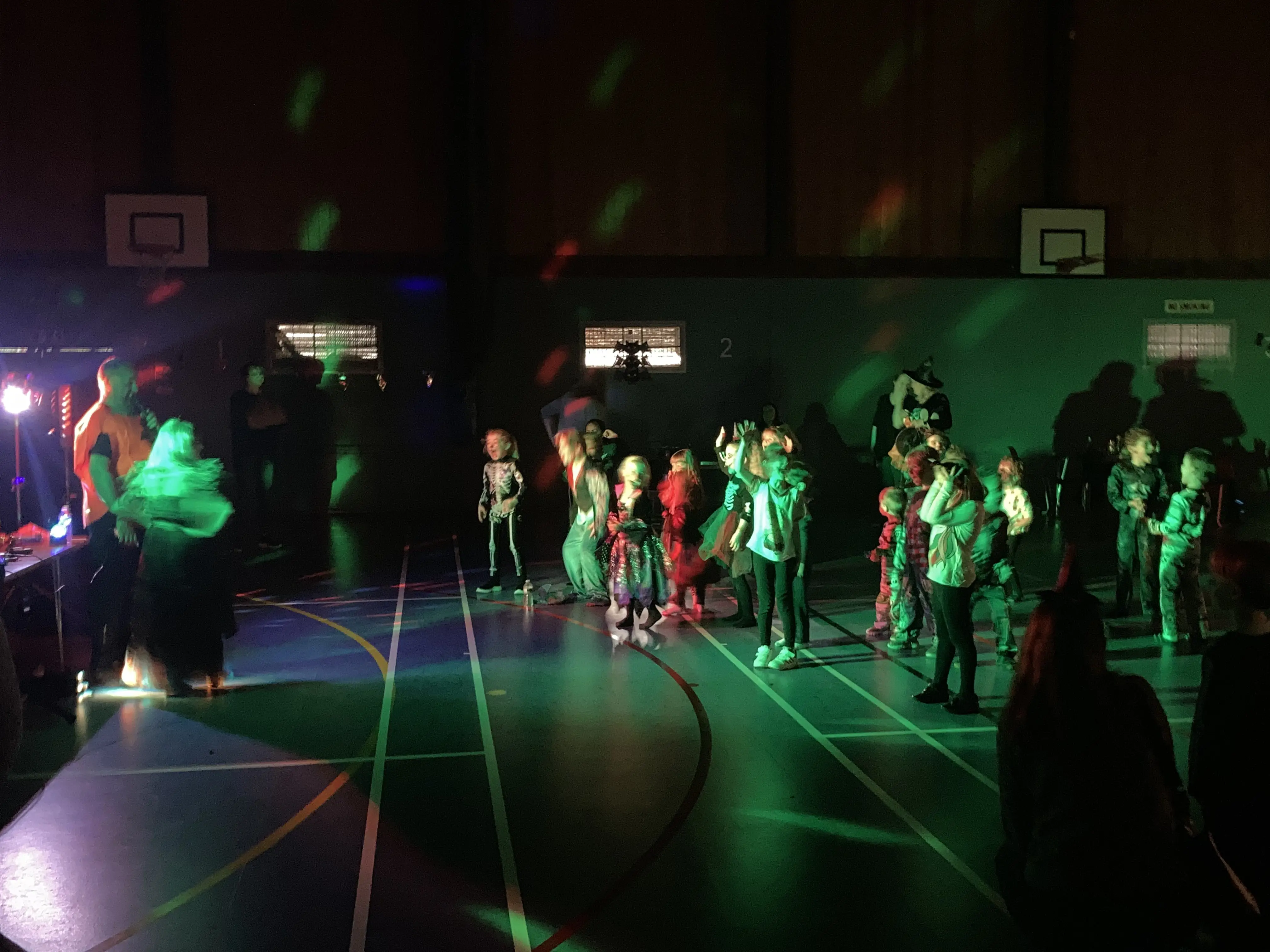 Kids dressed up in a sports hall for Halloween with lights turned down for spooky atmosphere