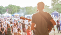 Man singing and playing guitar on stage, looking out at audience preview