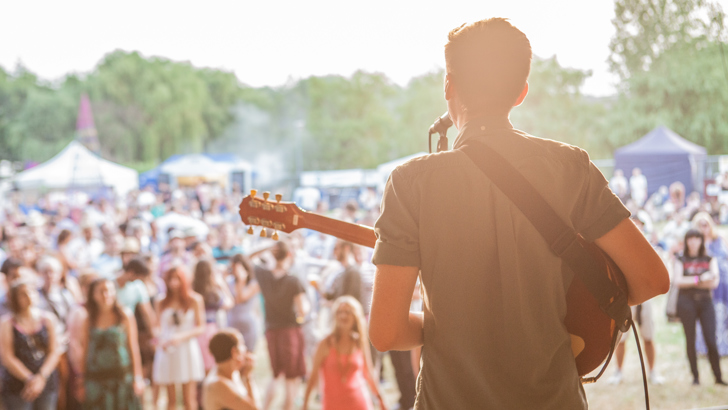 Man singing and playing guitar on stage, looking out at audience
