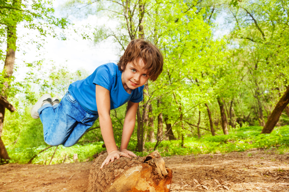 Boy in forest jumping over tree trunk