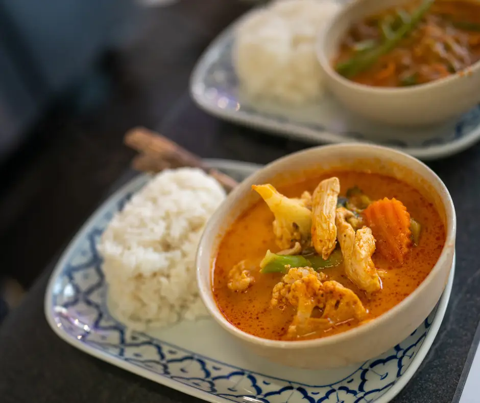 Bowl of curry served in bowl, resting on blue and white plate with white rice on it