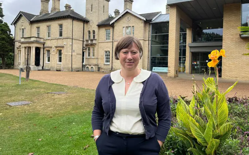 A woman with short brown hair smiles at the camera while stood outside of Chelmsford Museum. 